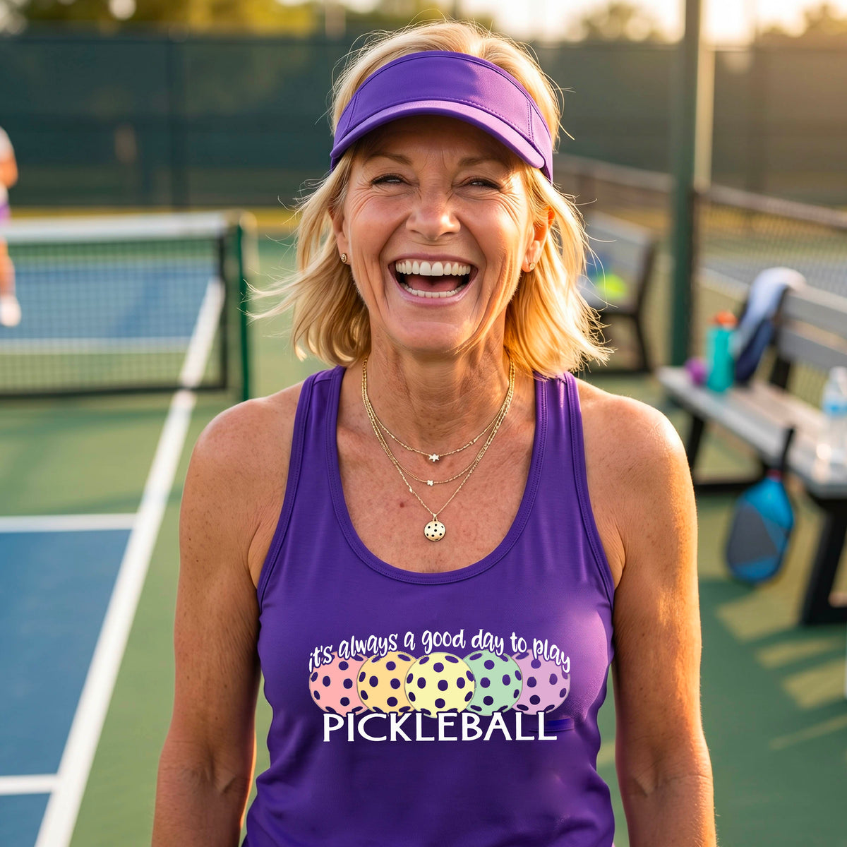A woman n a pickleball court wearing a hot purple racerback tank top with a colorful pickleball graphic and the text 'It's always a good day to play PICKLEBALL'.