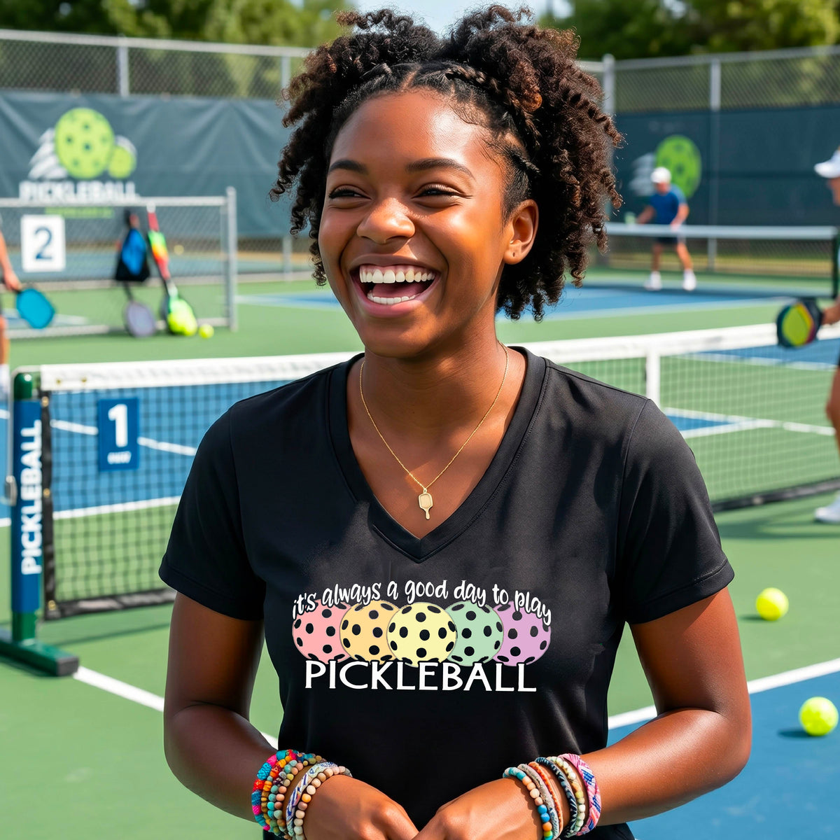 A woman wearing a bright black V-neck t-shirt with a colorful graphic that reads 'it's always a good day to play PICKLEBALL' and coloful pickleballs.