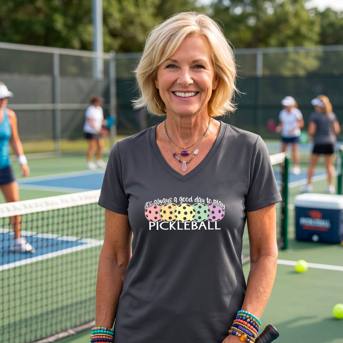 A woman wearing a gray V-neck t-shirt with a colorful graphic that reads 'it's always a good day to play PICKLEBALL' and coloful pickleballs.