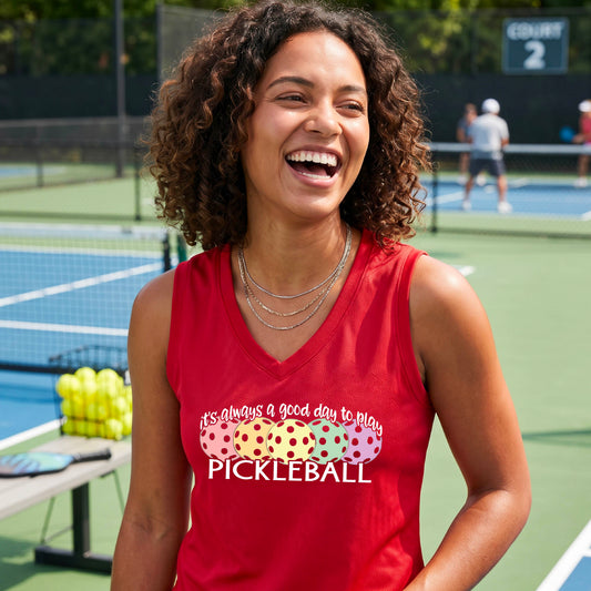 A woman smiling on a pickleball court, wearing a red sleeveless tank top with a colorful pickleball graphic and the text 'it's always a good day to play PICKLEBALL'.