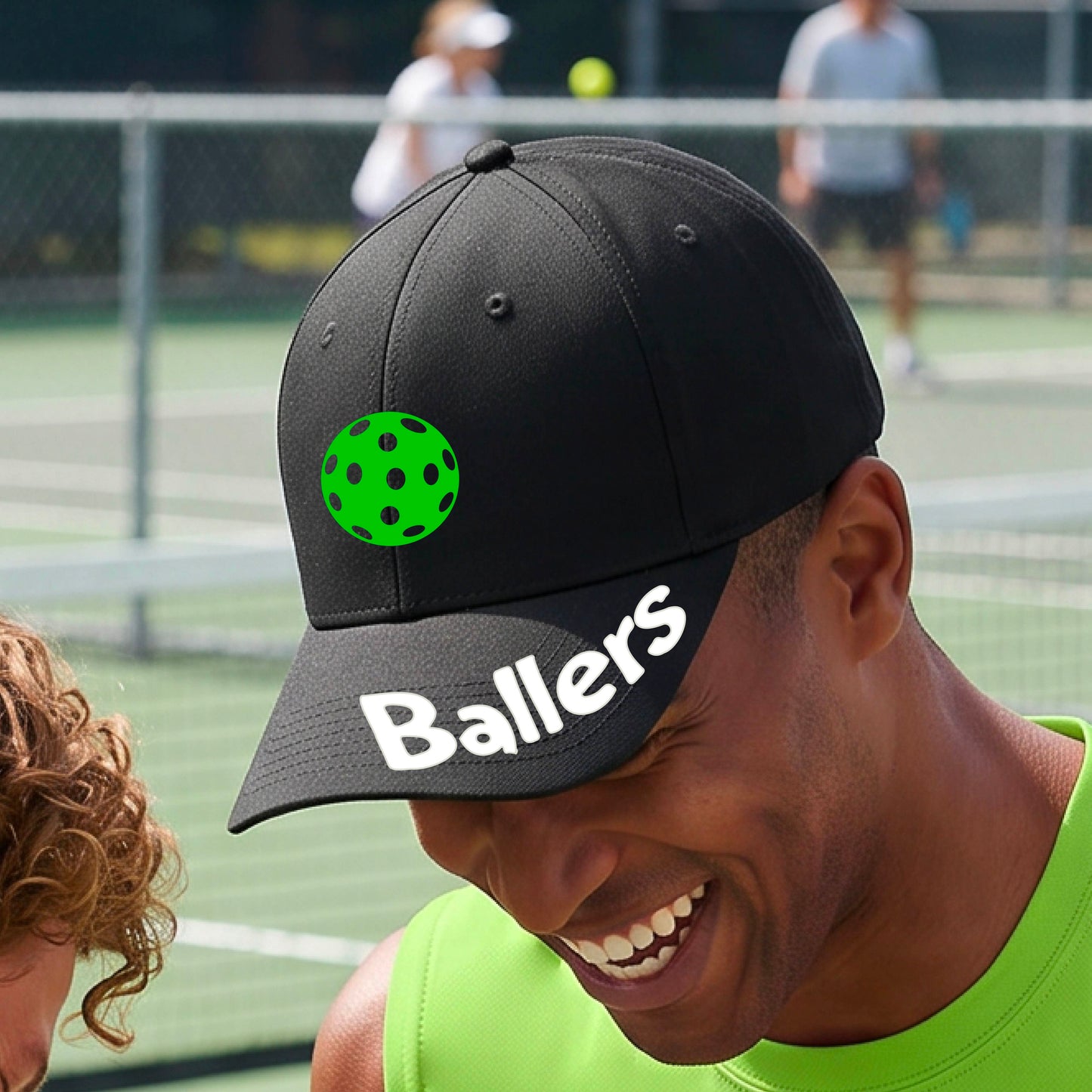 A close up of a black baseball cap with a pickleball graphic on the front and the word 'Ballers' in white on the brim.