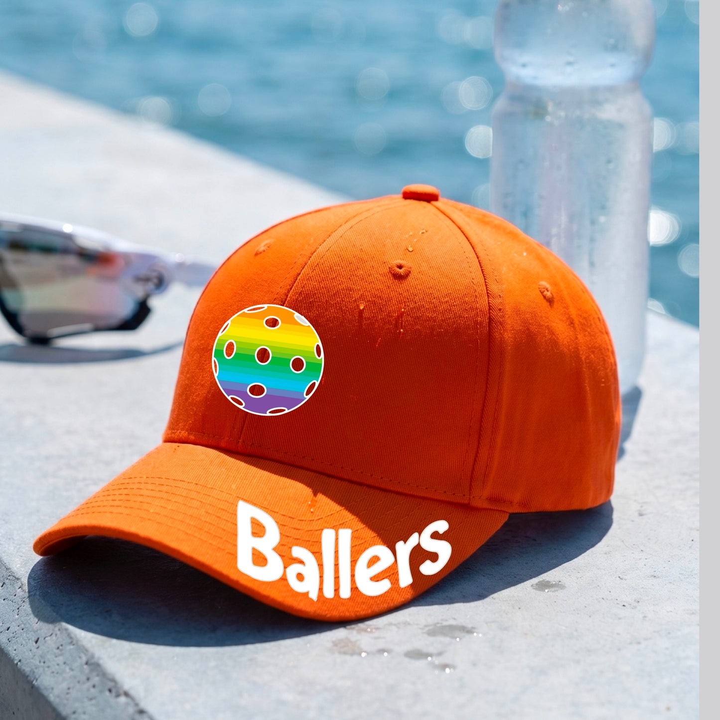 A close up of an orange baseball cap with a pickleall graphic on the front and the word 'Ballers' in white on the brim.