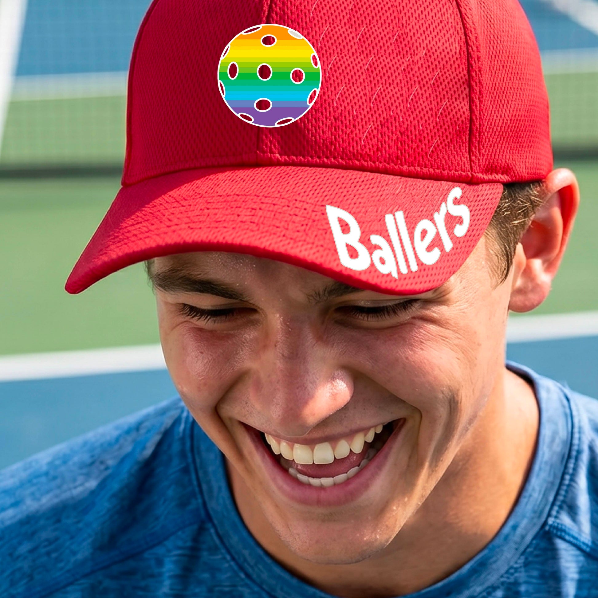 A close up of a red baseball cap with a pickleball graphic on the front and the word 'Ballers' in white on the brim.