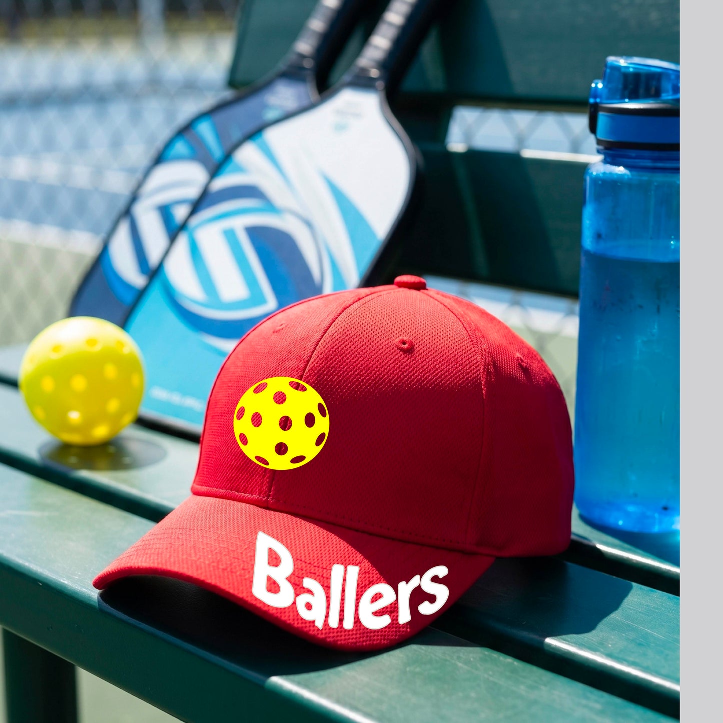 A close up of a red baseball cap with a pickleall graphic on the front and the word 'Ballers' in white on the brim.