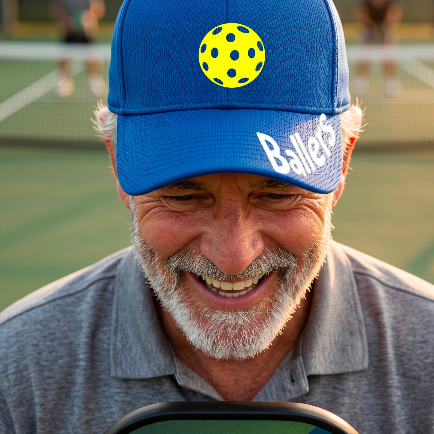 A person on a pickleball court wearing a royal blue baseball cap with a pickleball graphic on the front and the word 'Ballers' in white on the brim.