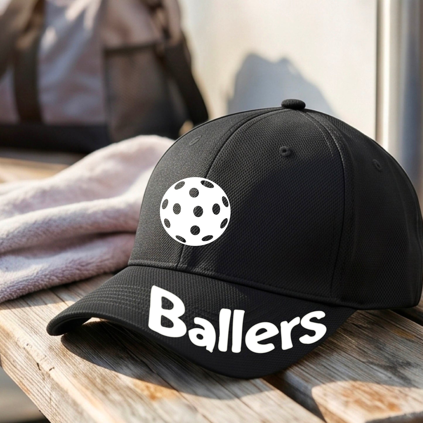 A close up of a black baseball cap with a pickleall graphic on the front and the word 'Ballers' in white on the brim.
