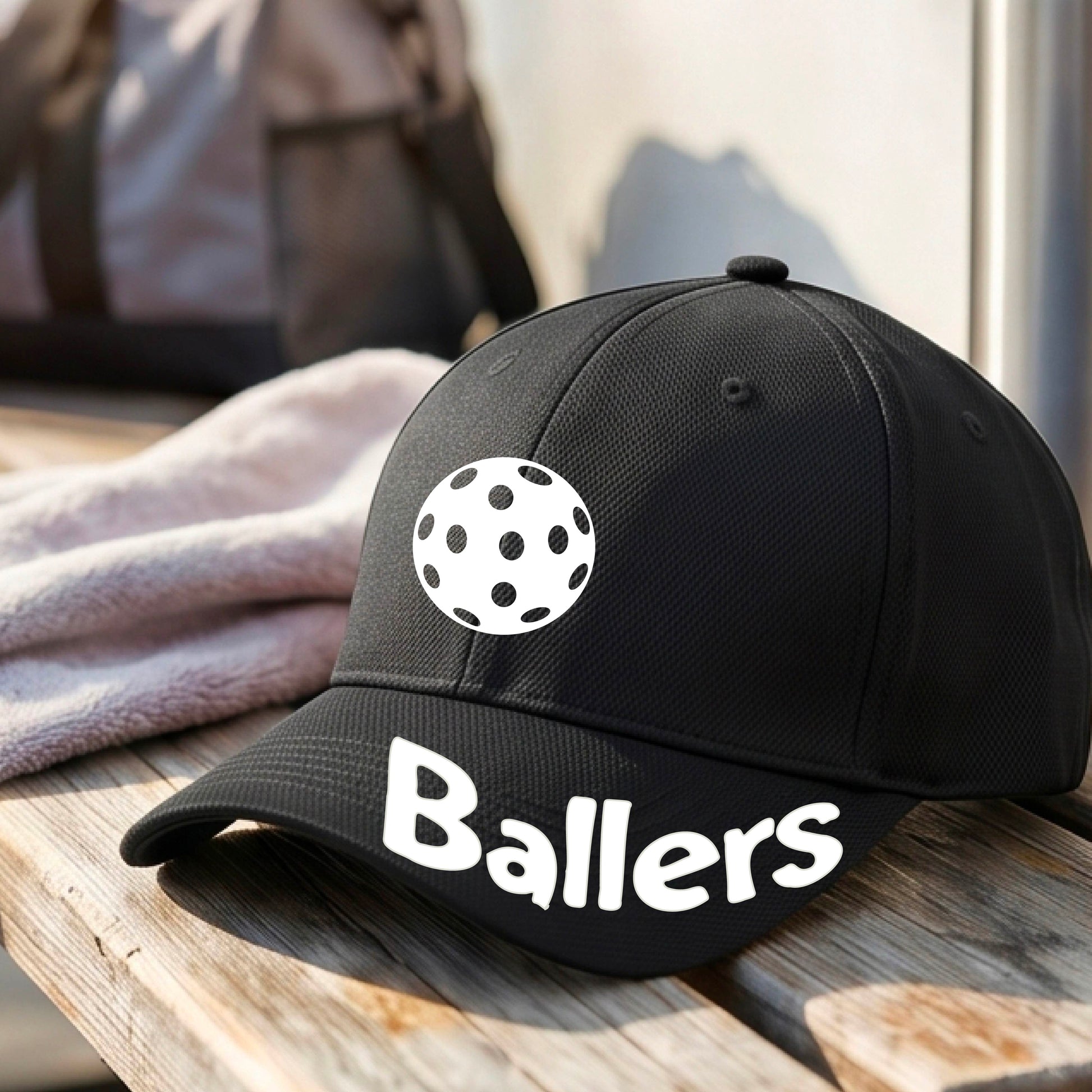 A close up of a black baseball cap with a pickleall graphic on the front and the word 'Ballers' in white on the brim.