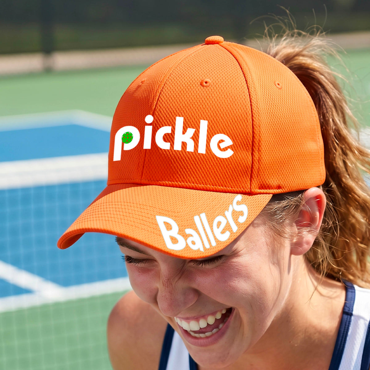 A close up of an orange mid-profile pickleball baseball cap with the text 'pickle' across the front and 'ballers' curved on the brim. 