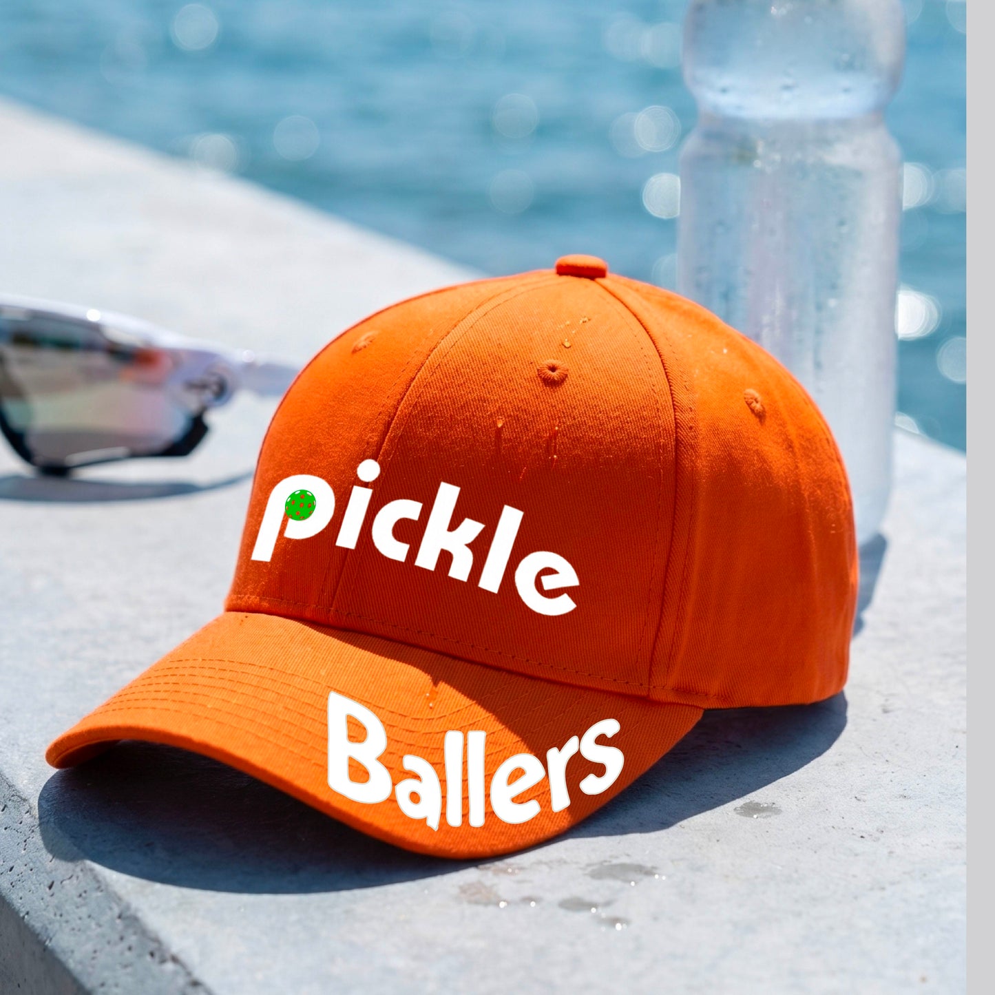 A close up of an orange mid-profile pickleball baseball cap with the text 'pickle' across the front and 'ballers' curved on the brim. 