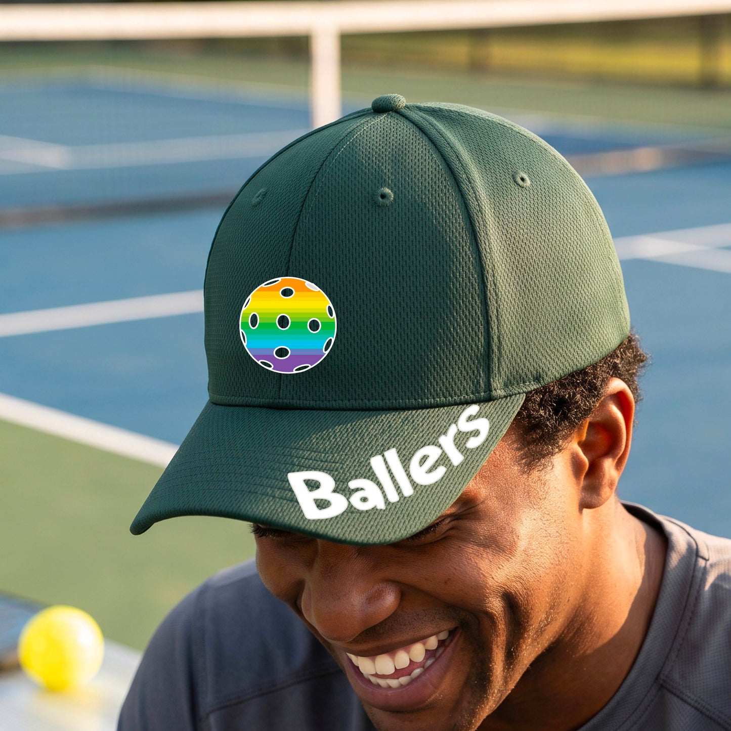 A person on a pickleball court wearing a green baseball cap with a pickleball graphic on the front and the word 'Ballers' in white on the brim.