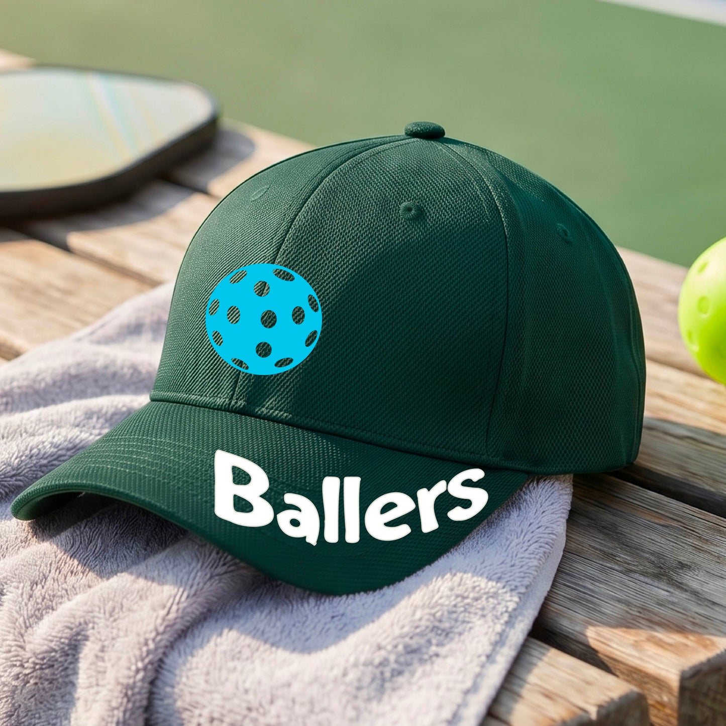 A close up of a green baseball cap with a pickleall graphic on the front and the word 'Ballers' in white on the brim.