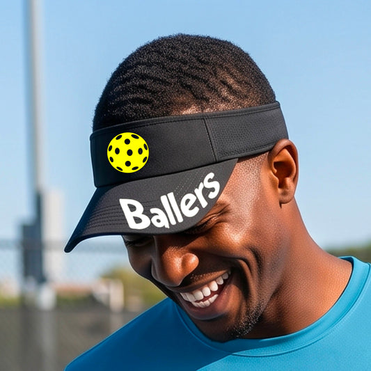 A person wearing a black visor with a yellow pickleball graphic and the word 'Ballers' in white,.