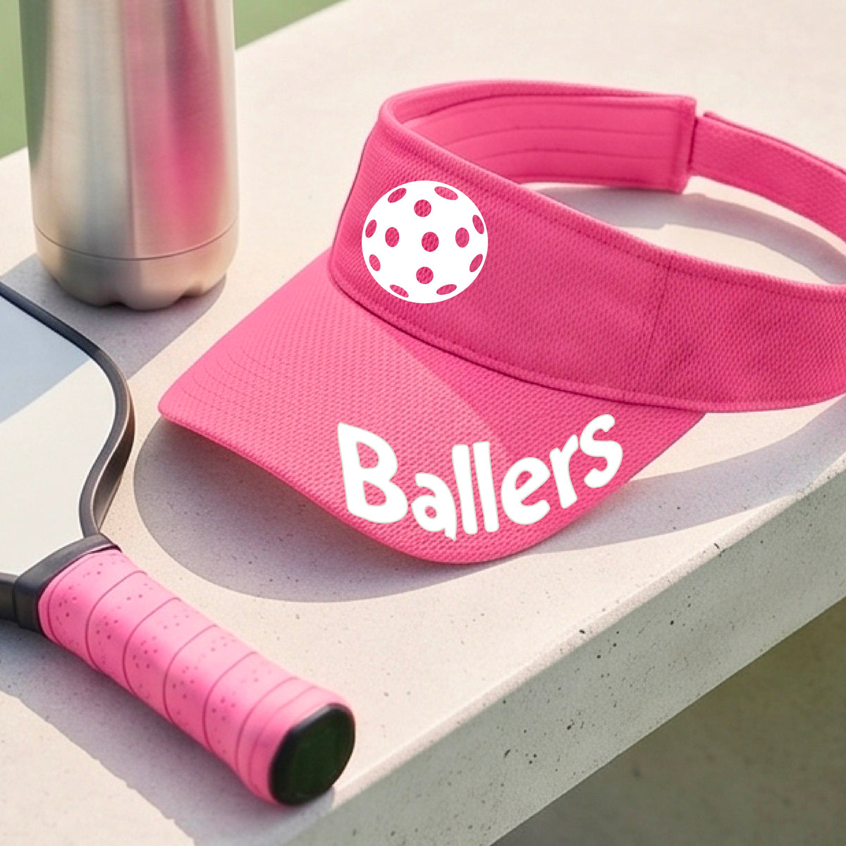 A close up of a pink visor with pickleball graphic and the word 'Ballers' in white,.