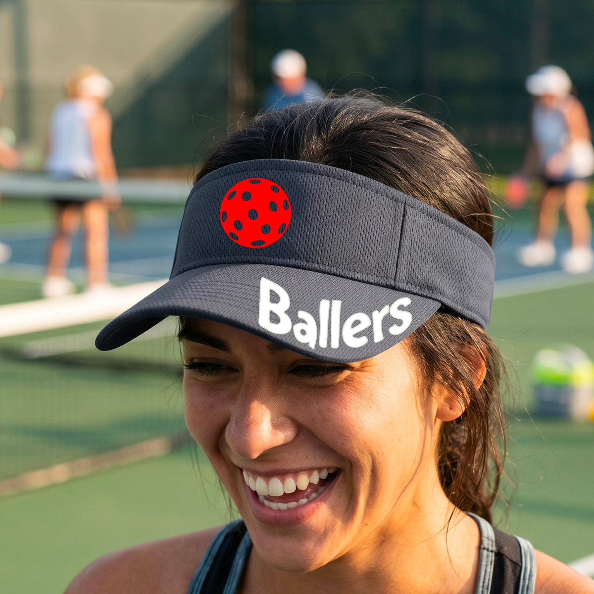 A person wearing a graphite gray visor with a yellow pickleball graphic and the word 'Ballers' in white,.