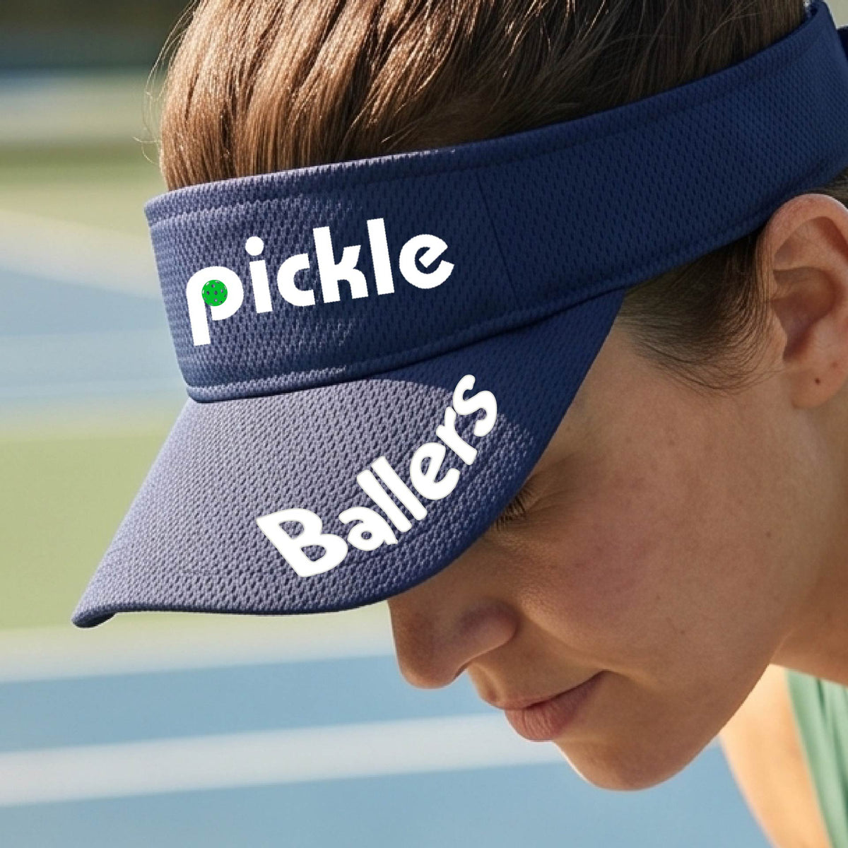 A close up of a navy blue visor with a pickleball graphic of 'pickle' and 'Ballers' printed in white on the front and brim.