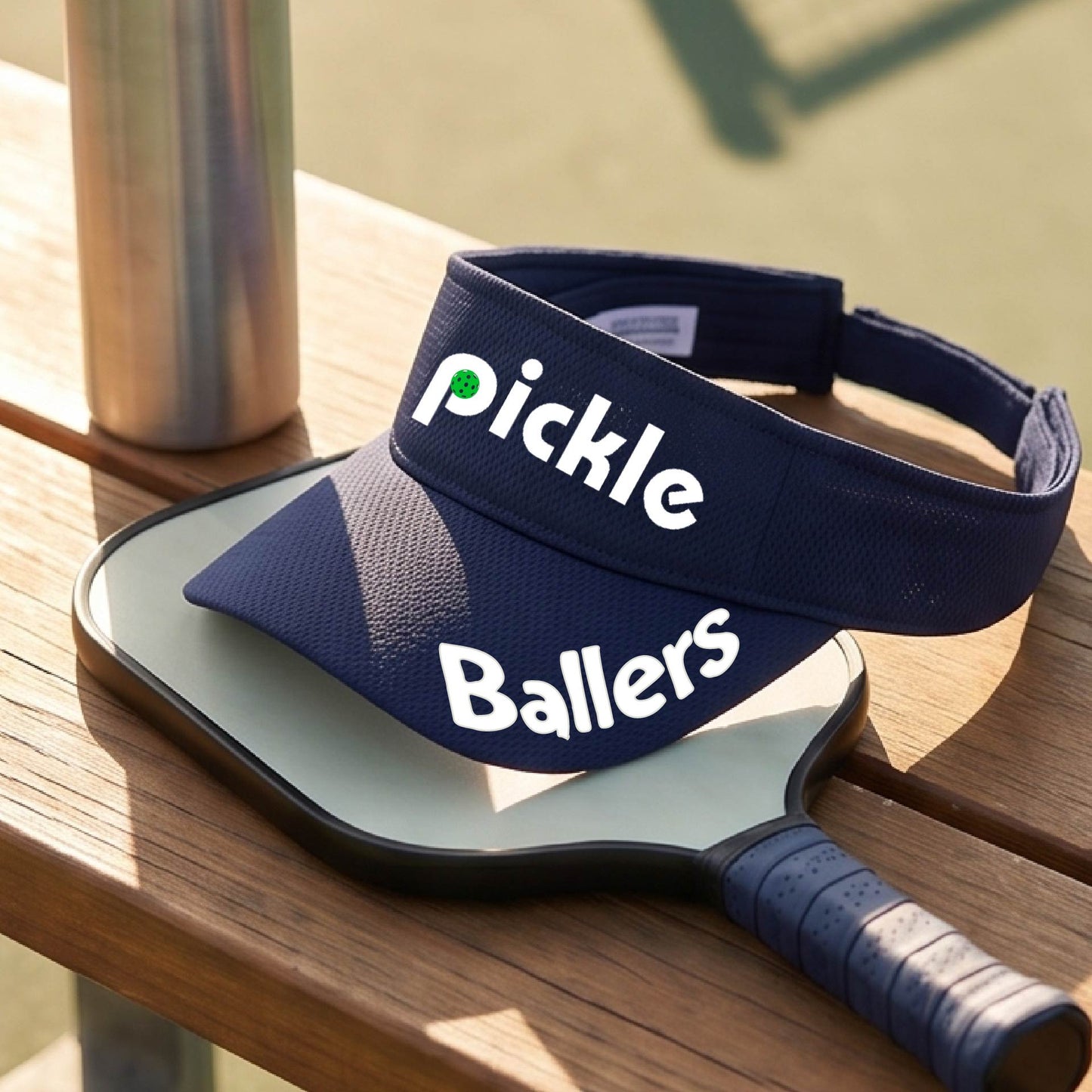 A close up of a navy blue visor with a pickleball graphic of 'pickle' and 'Ballers' printed in white on the front and brim.