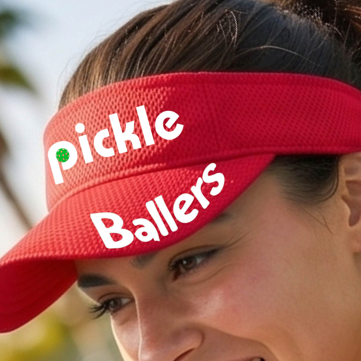 A close up of a red visor with a pickleball graphic of 'pickle' and 'Ballers' printed in white on the front and brim.