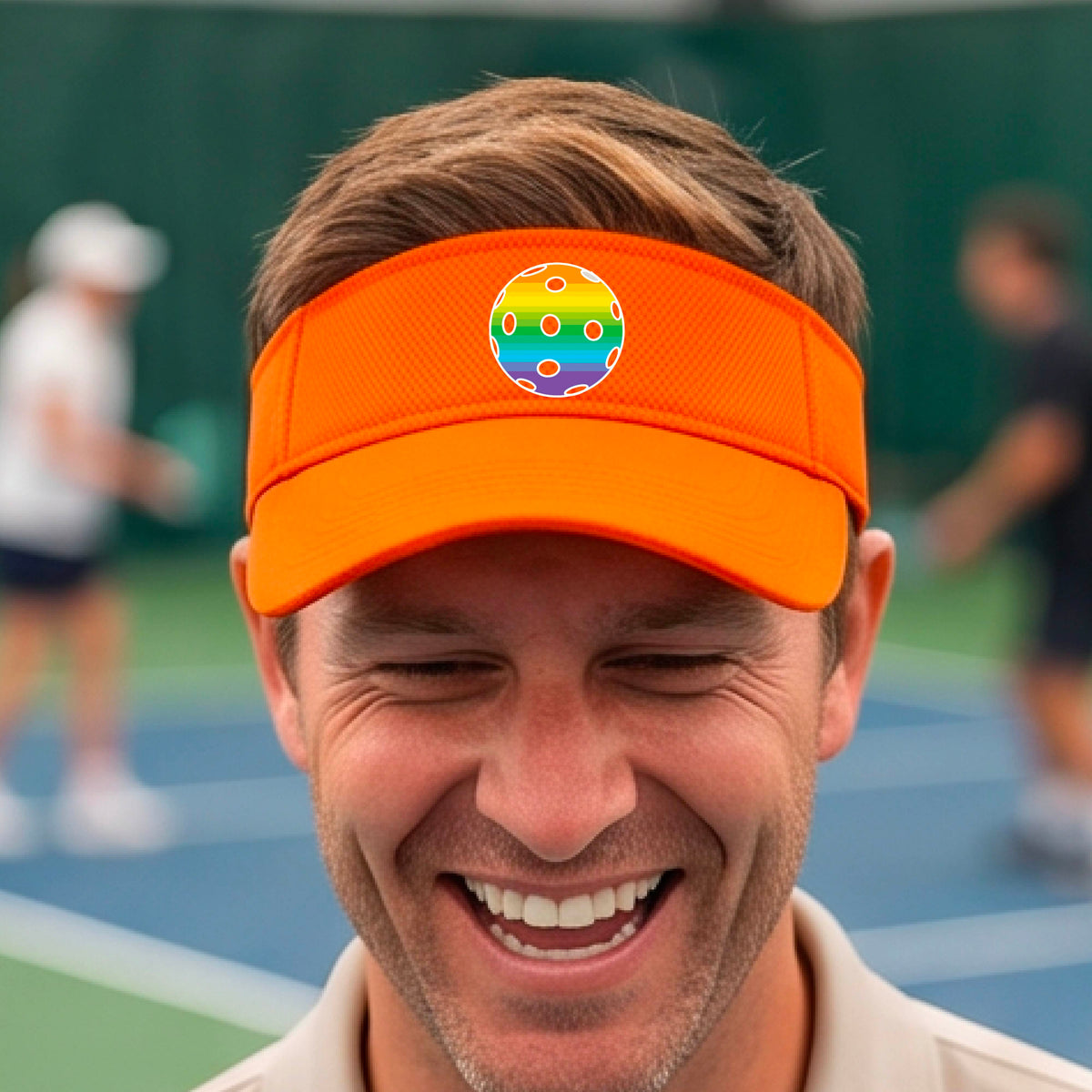 A close-up of a person  wearing an orange visor with a pickleball graphic, set against a blurred pickleball court background.