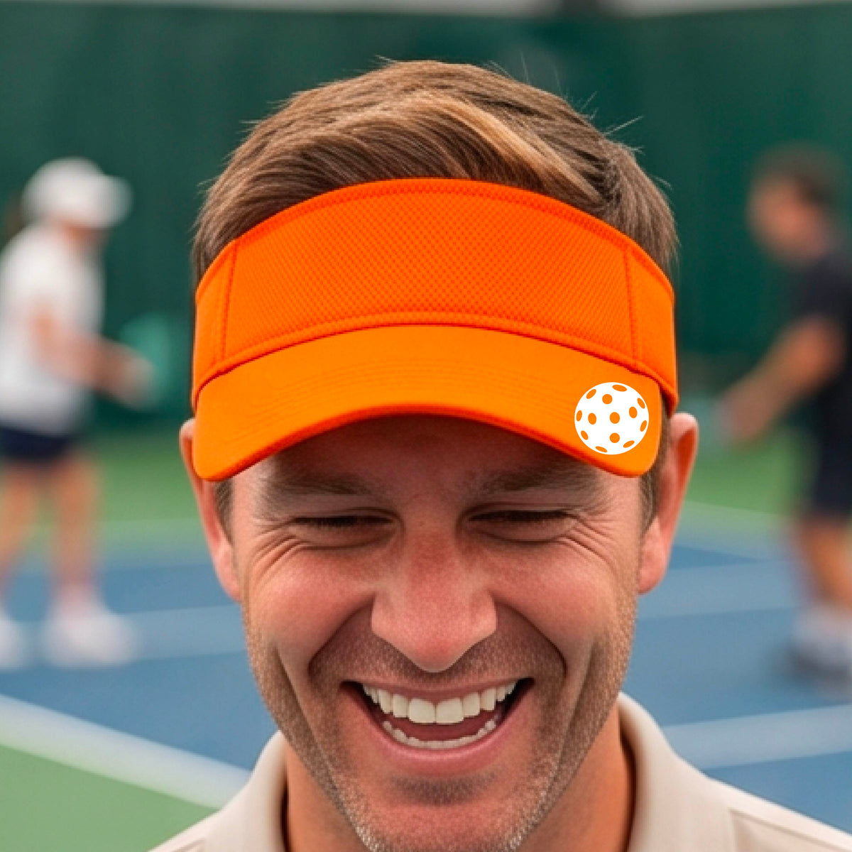 A close-up of a person  wearing a orange visor with a pickleball graphic, set against a blurred pickleball court background.
