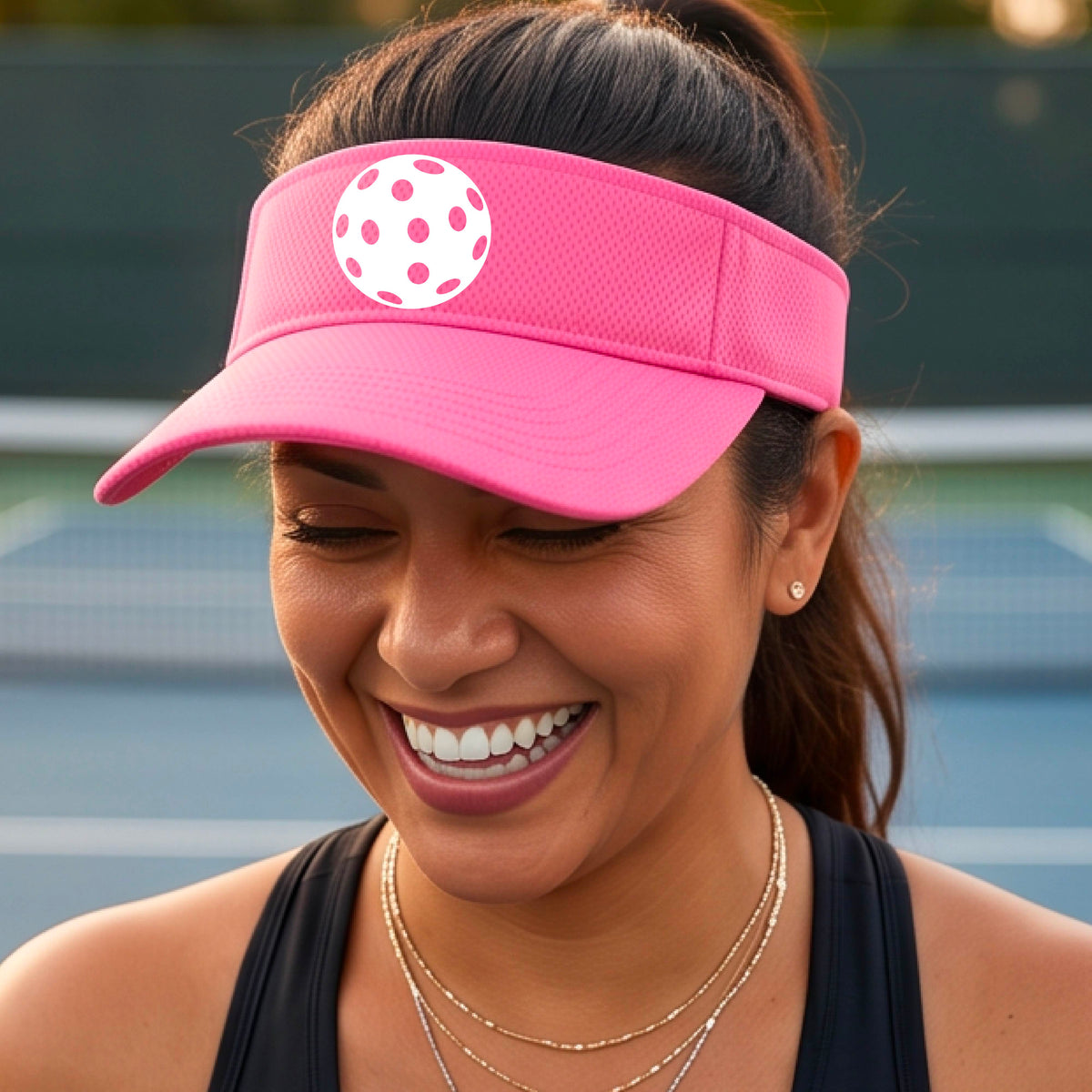 A close-up of a person  wearing a pink visor with a pickleball graphic, set against a blurred pickleball court background.