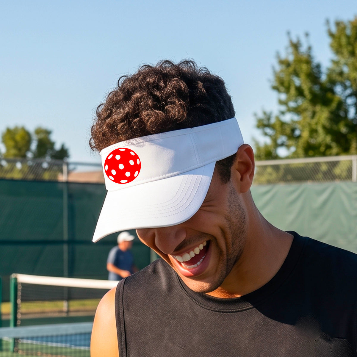 A close-up of a person  wearing a white visor with a pickleball graphic, set against a blurred pickleball court background.