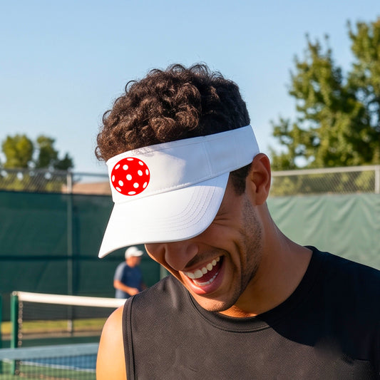 A close-up of a person  wearing a white visor with a pickleball graphic, set against a blurred pickleball court background.