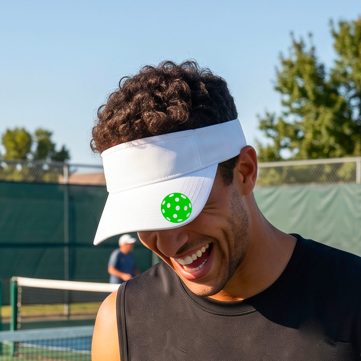 A close-up of a person  wearing a white visor with a pickleball graphic, set against a blurred pickleball court background.