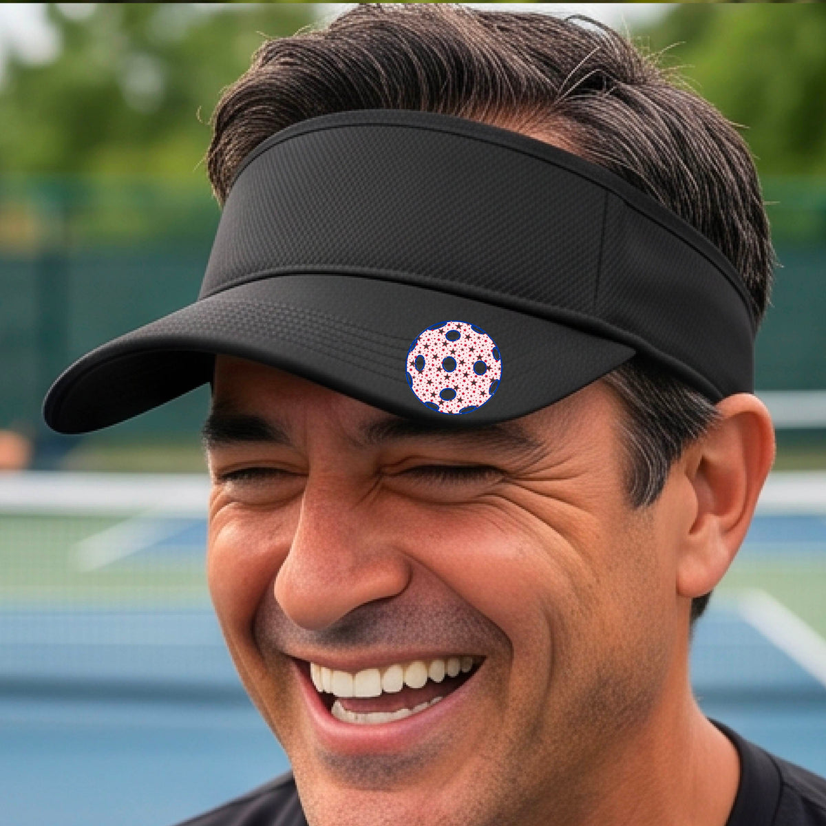 A close-up of a person  wearing a black visor with a pickleball graphic, set against a blurred pickleball court background.