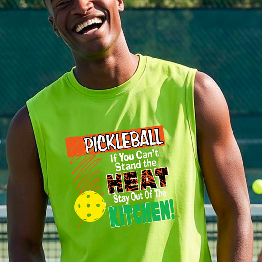 A man wearing a bright neon yellow-green sleeveless t-shirt with a colorful pickleball graphic and text on the front, “If You Can't Stand The Heat Stay Out Of The Kitchen" set against a blurred outdoor pickleball court background.