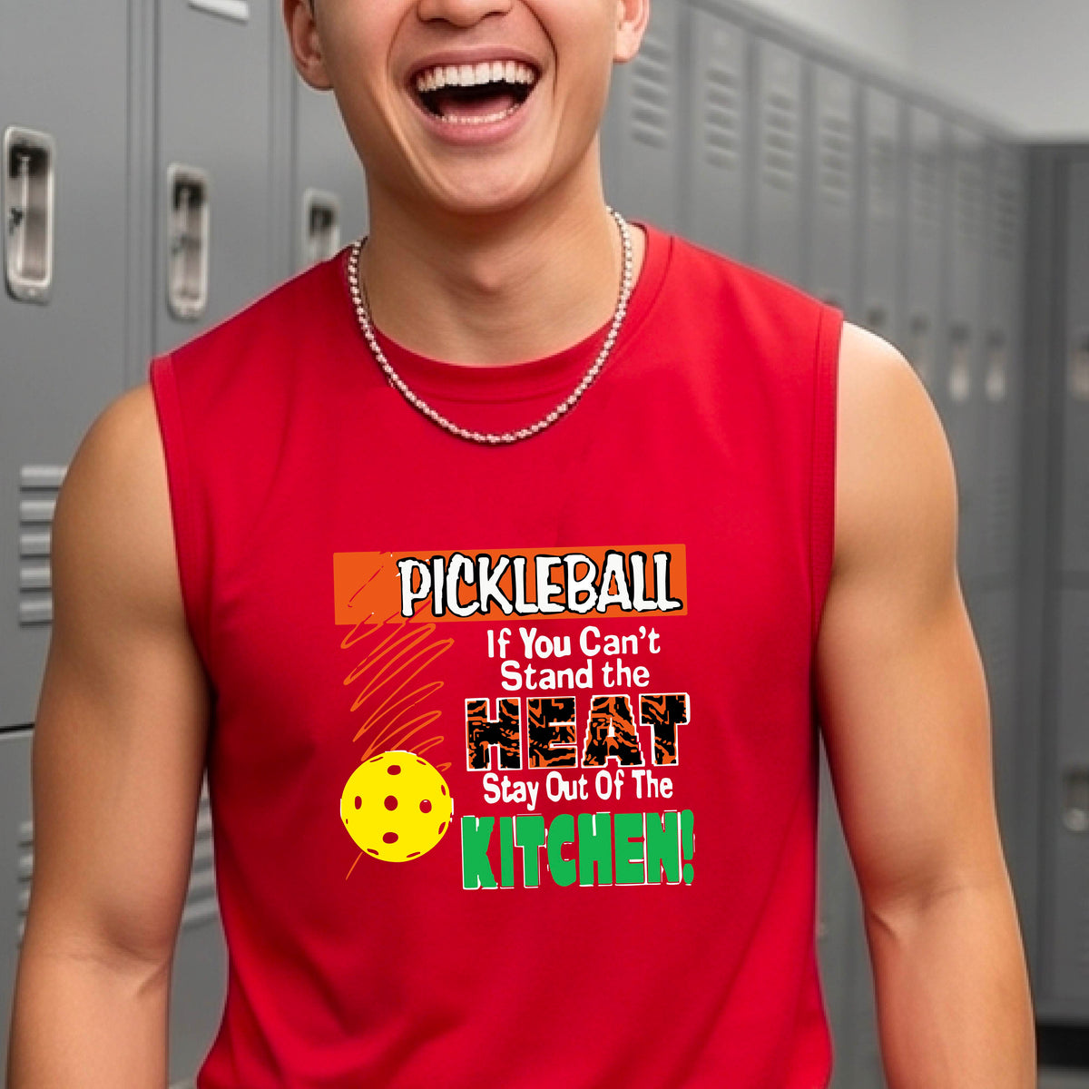 A man wearing a bright red sleeveless t-shirt with a colorful pickleball graphic and text on the front, “If You Can't Stand The Heat Stay Out Of The Kitchen" set against a blurred outdoor pickleball court background.