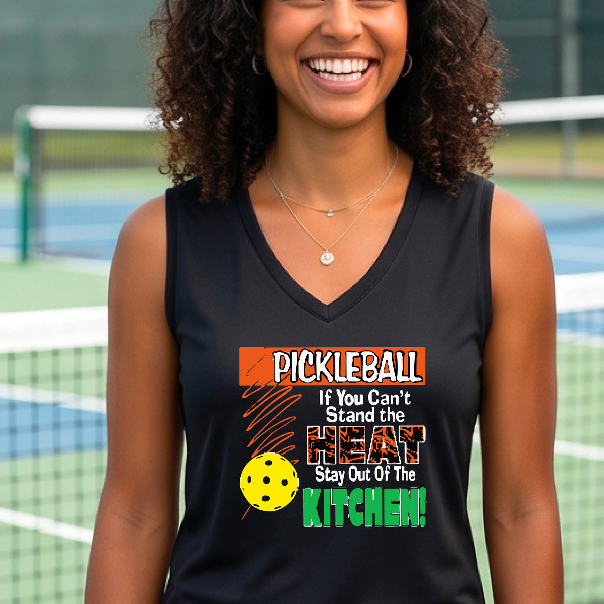 A close up of a black sleeveless V-neck tank top with a colorful pickleball graphic and text on the front "IF YOU CAN'T STAND THE HEAT STAY OUT OF THE KITCHEN."