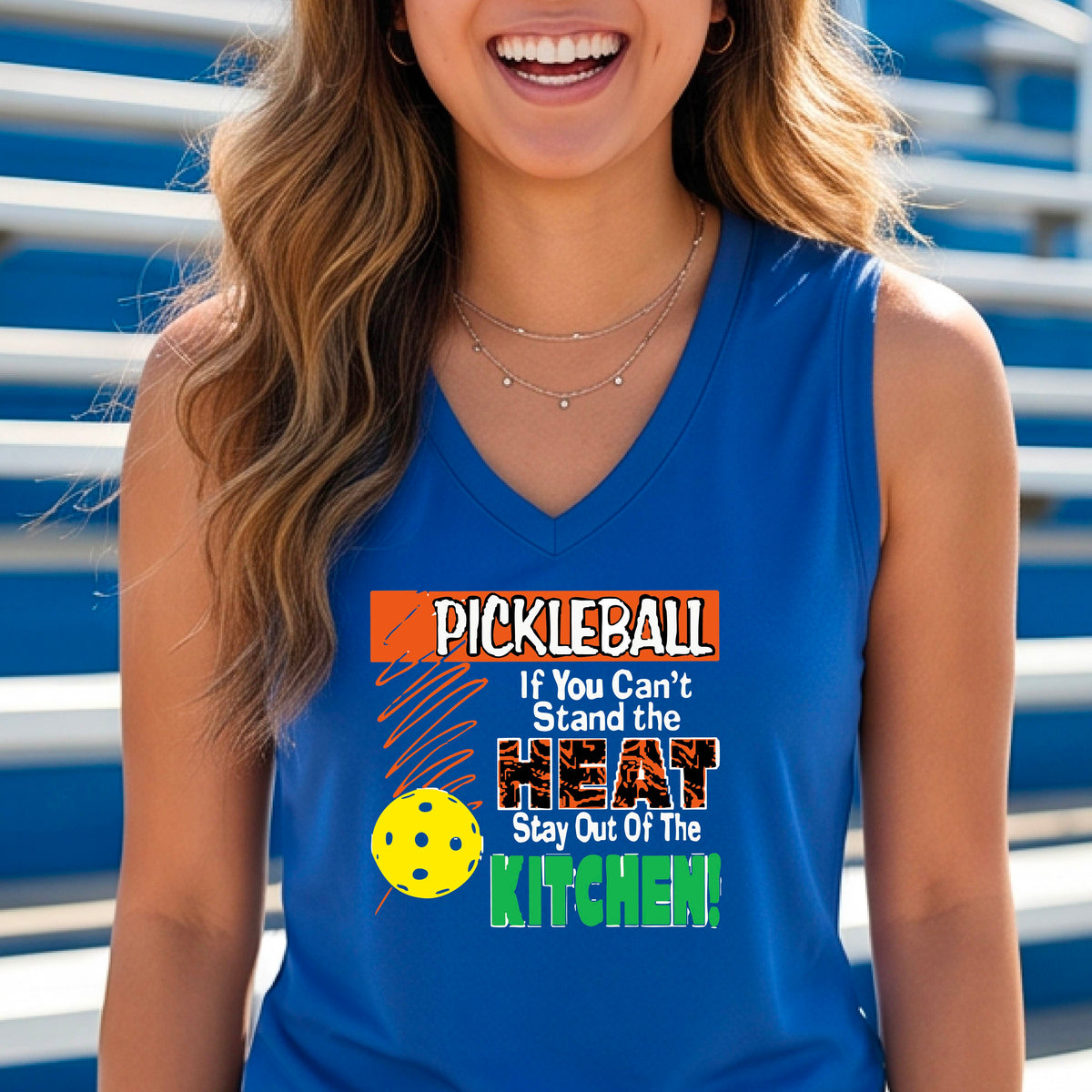 A close up of a bright blue sleeveless V-neck tank top with a colorful pickleball graphic and text on the front "IF YOU CAN'T STAND THE HEAT STAY OUT OF THE KITCHEN."