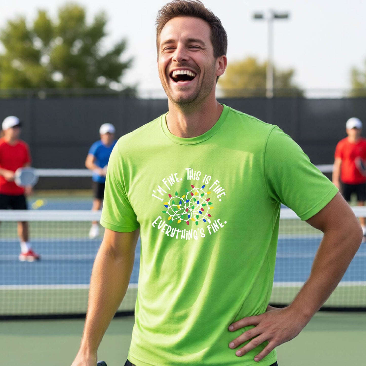 A man smiling on an pickleball court wearing a bright lime green t-shirt with a colorful graphic of tangeled Christmas lights and the text 'I'M FINE. THIS IS FINE. EVERYTHING'S FINE.'