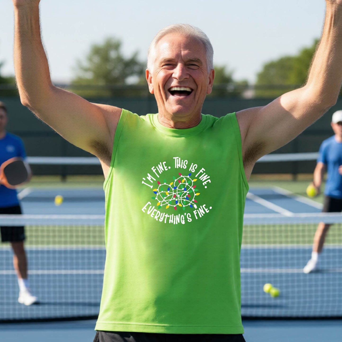 A smiling male wearing a lime green sleeveless t-shirt with a pickleball court in the background.  The shirt has a graphic of a tangled string of christmas lights witht the words 'I'M FINE. THIS IS FINE. EVERYTHING'S FINE.