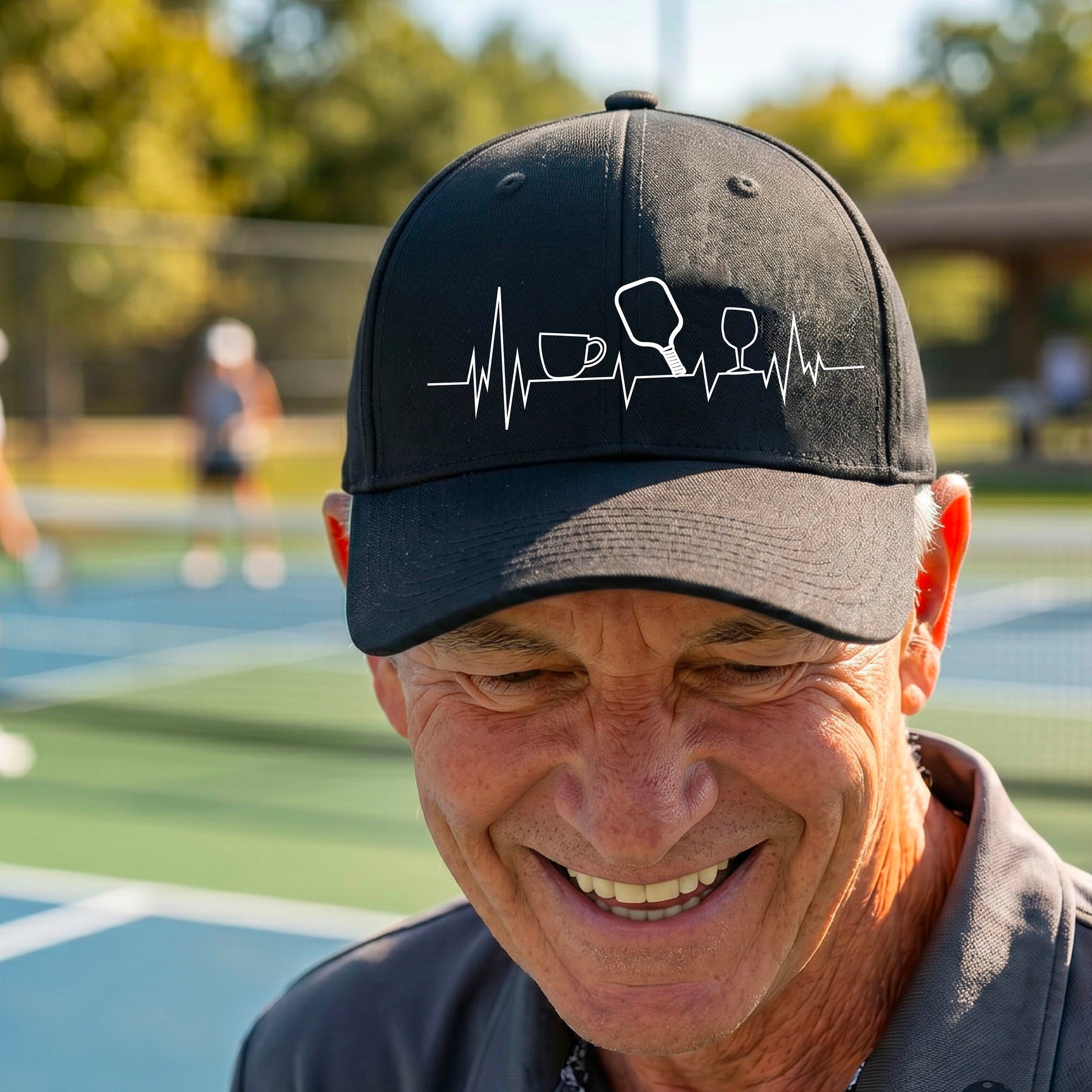 A close up of a  pickleball visor with  a white line-art graphic of a coffee cup, pickleball paddle and a wine glass, on a heartbeat EKG line.