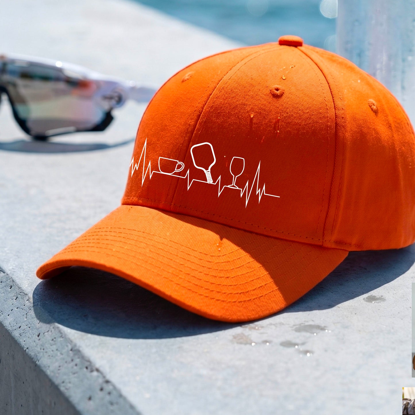 A close up of an orange pickleball visor with  a white line-art graphic of a coffee cup, pickleball paddle and a wine glass, on a heartbeat EKG line.