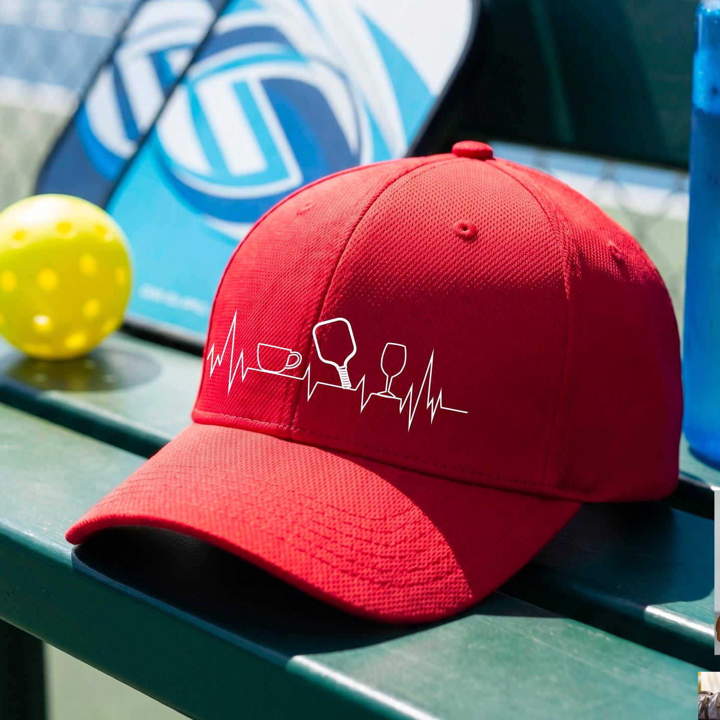 A close up of a red pickleball visor with  a white line-art graphic of a coffee cup, pickleball paddle and a wine glass, on a heartbeat EKG line.