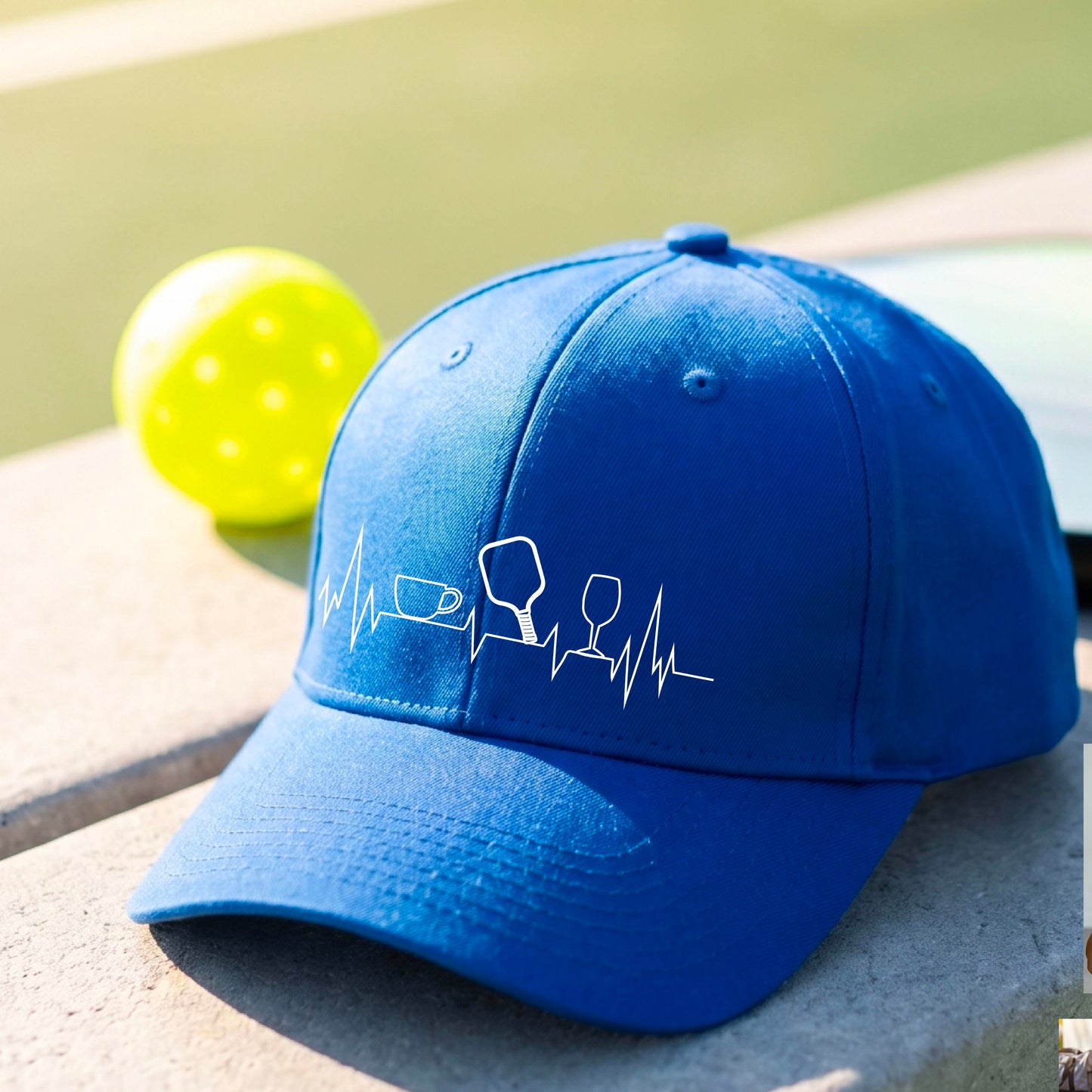 A close up of a royal blue pickleball visor with  a white line-art graphic of a coffee cup, pickleball paddle and a wine glass, on a heartbeat EKG line.