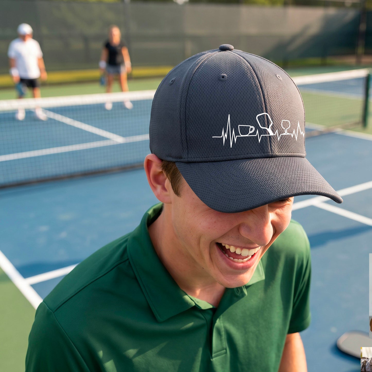 A close up of a gray pickleball visor with  a white line-art graphic of a coffee cup, pickleball paddle and a wine glass, on a heartbeat EKG line.