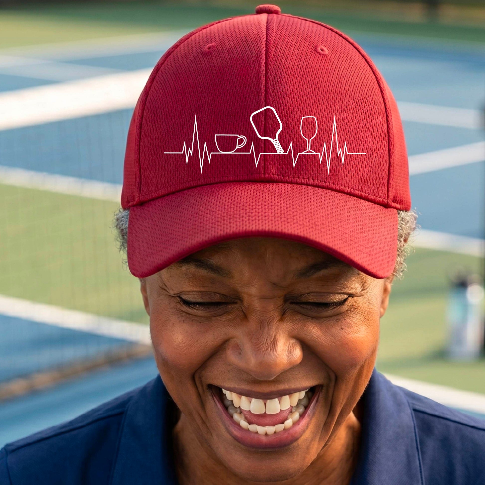 A close up of a red pickleball visor with  a white line-art graphic of a coffee cup, pickleball paddle and a wine glass, on a heartbeat EKG line.