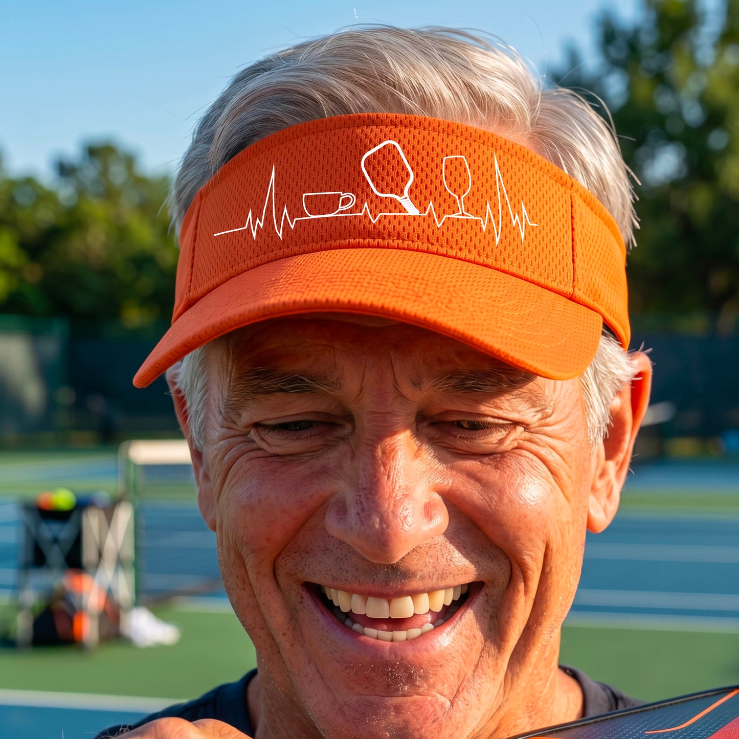 A close up of an orange pickleball visor with  a white line-art graphic of a coffee cup, pickleball paddle and a wine glass, on a heartbeat EKG line.