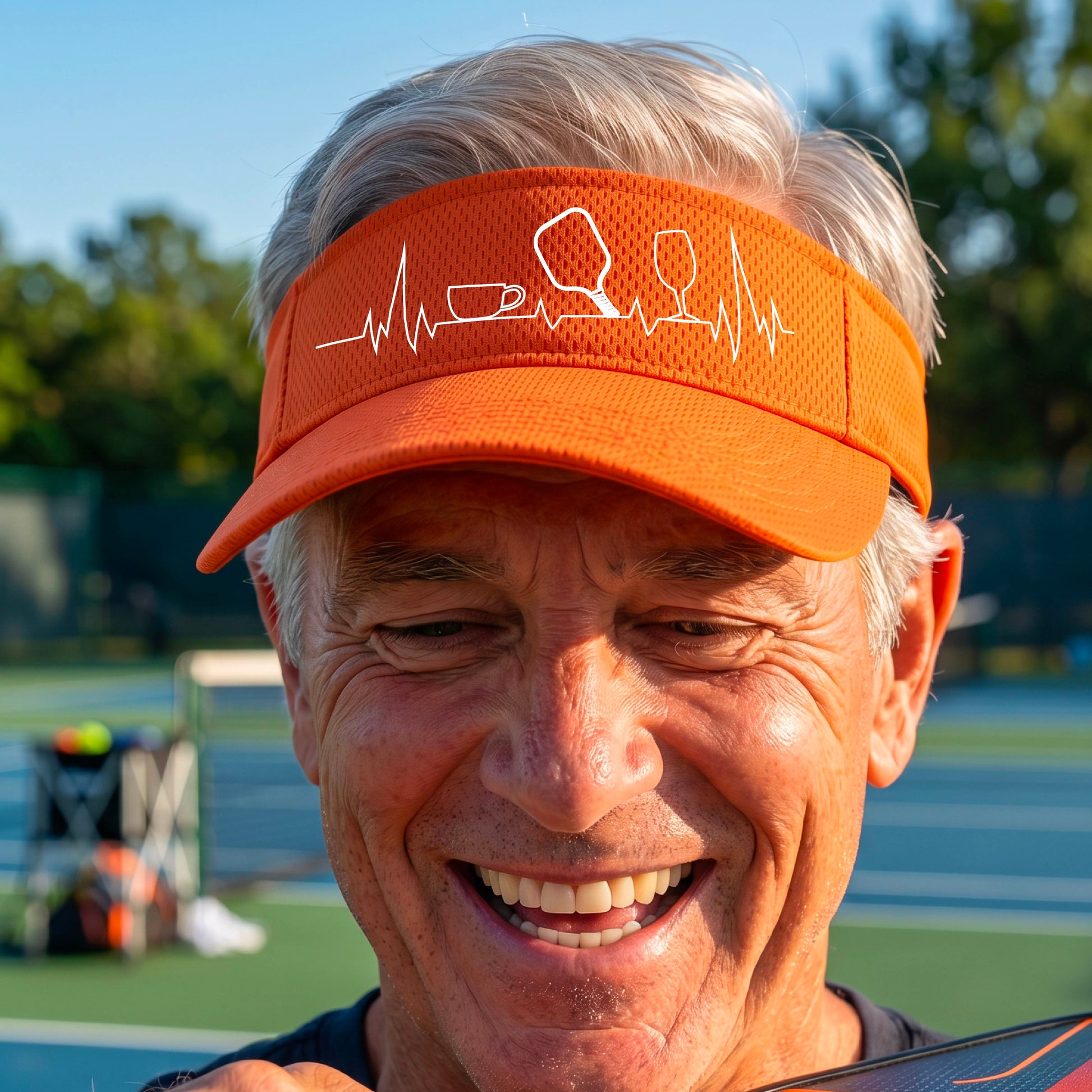 A close up of an orange pickleball visor with  a white line-art graphic of a coffee cup, pickleball paddle and a wine glass, on a heartbeat EKG line.
