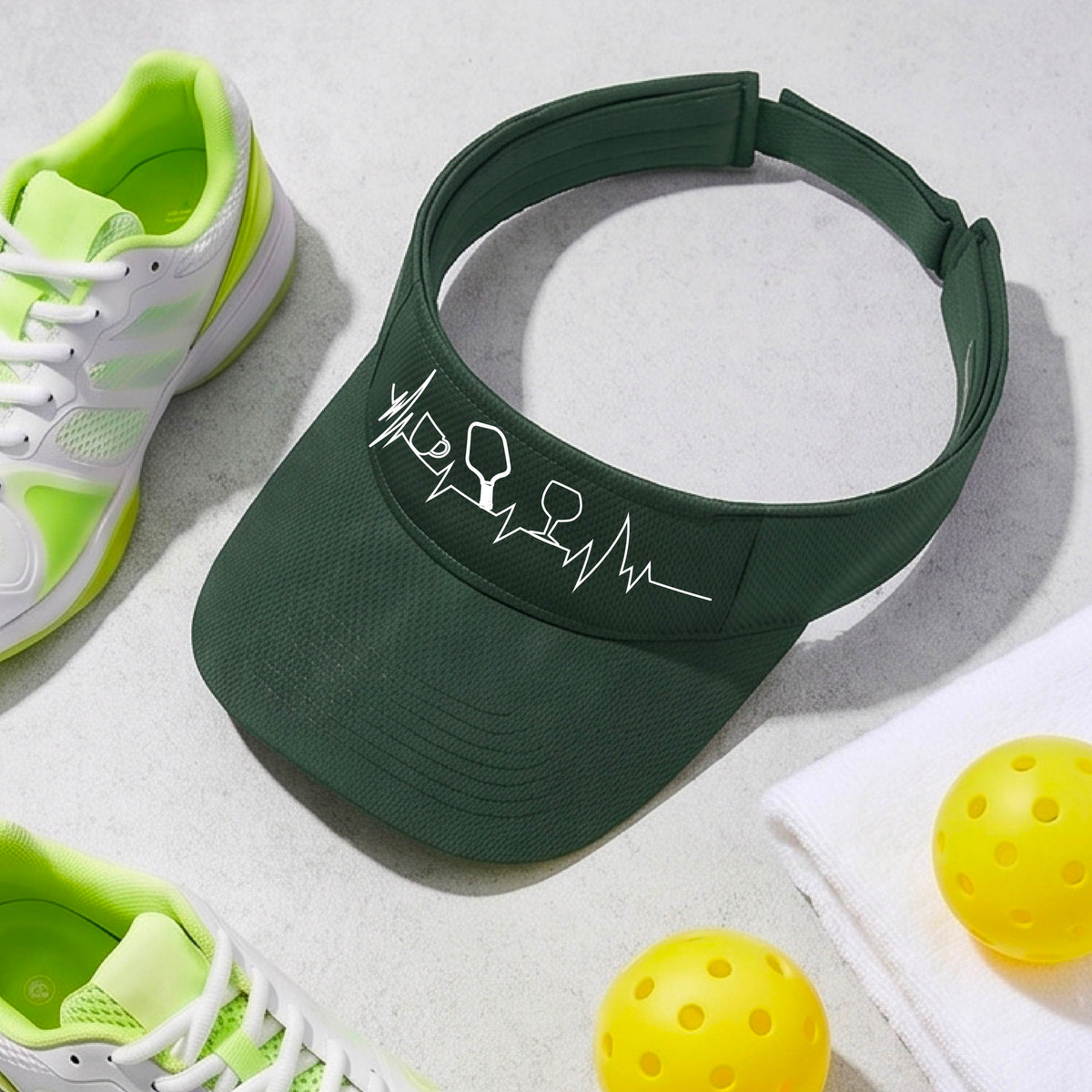 A close up of a green pickleball visor with  a white line-art graphic of a coffee cup, pickleball paddle and a wine glass, on a heartbeat EKG line.