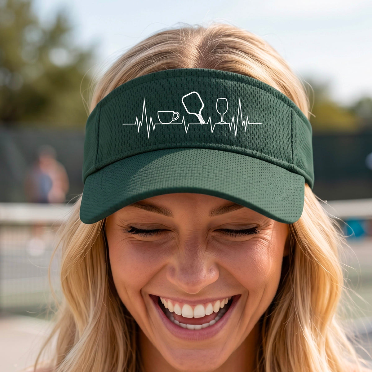 A close up of a green pickleball visor with  a white line-art graphic of a coffee cup, pickleball paddle and a wine glass, on a heartbeat EKG line.