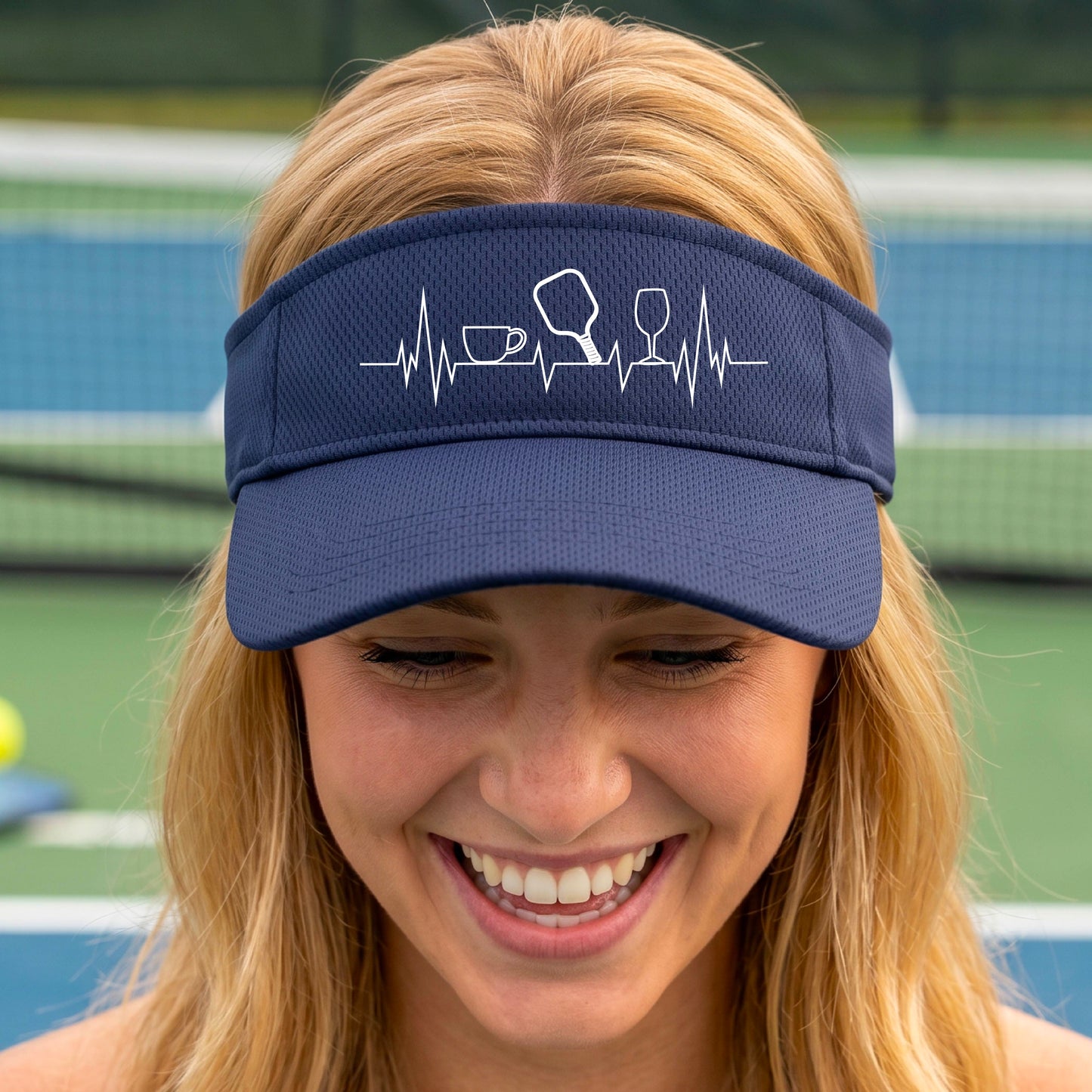 A close up of a navy blue pickleball visor with  a white line-art graphic of a coffee cup, pickleball paddle and a wine glass, on a heartbeat EKG line.