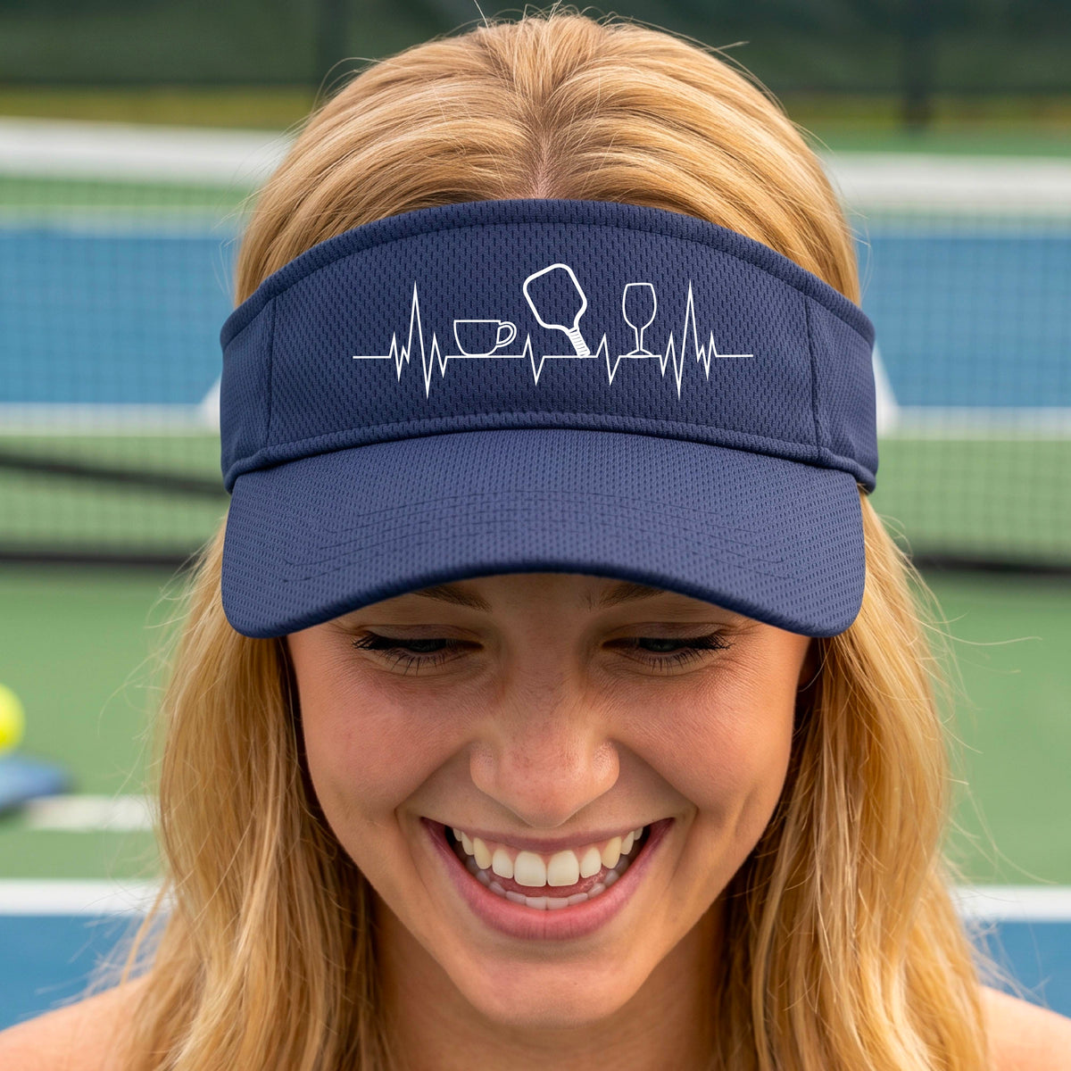 A close up of a navy blue pickleball visor with  a white line-art graphic of a coffee cup, pickleball paddle and a wine glass, on a heartbeat EKG line.