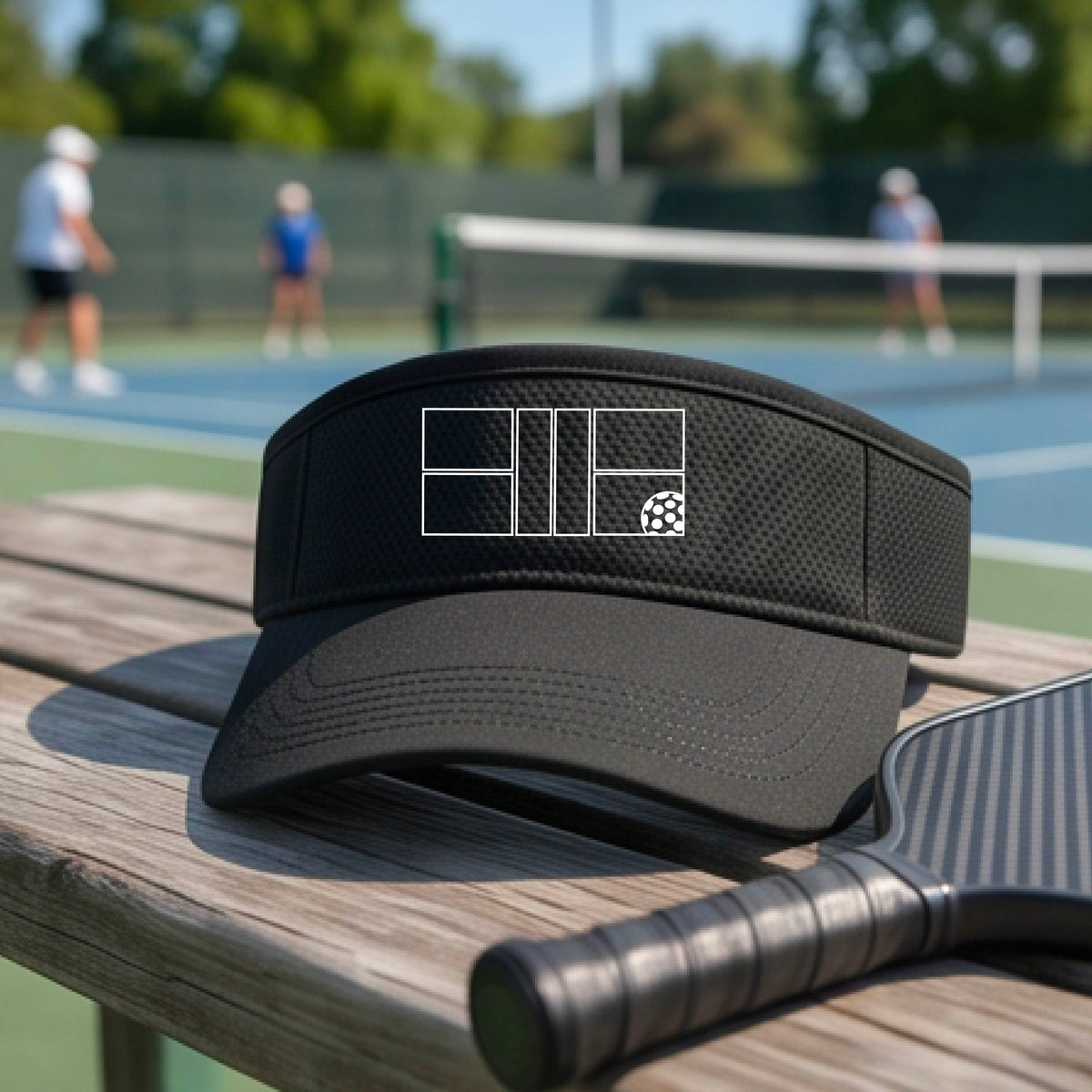 A close up of a black visor with a white pickleball court and ball graphic on the front. 