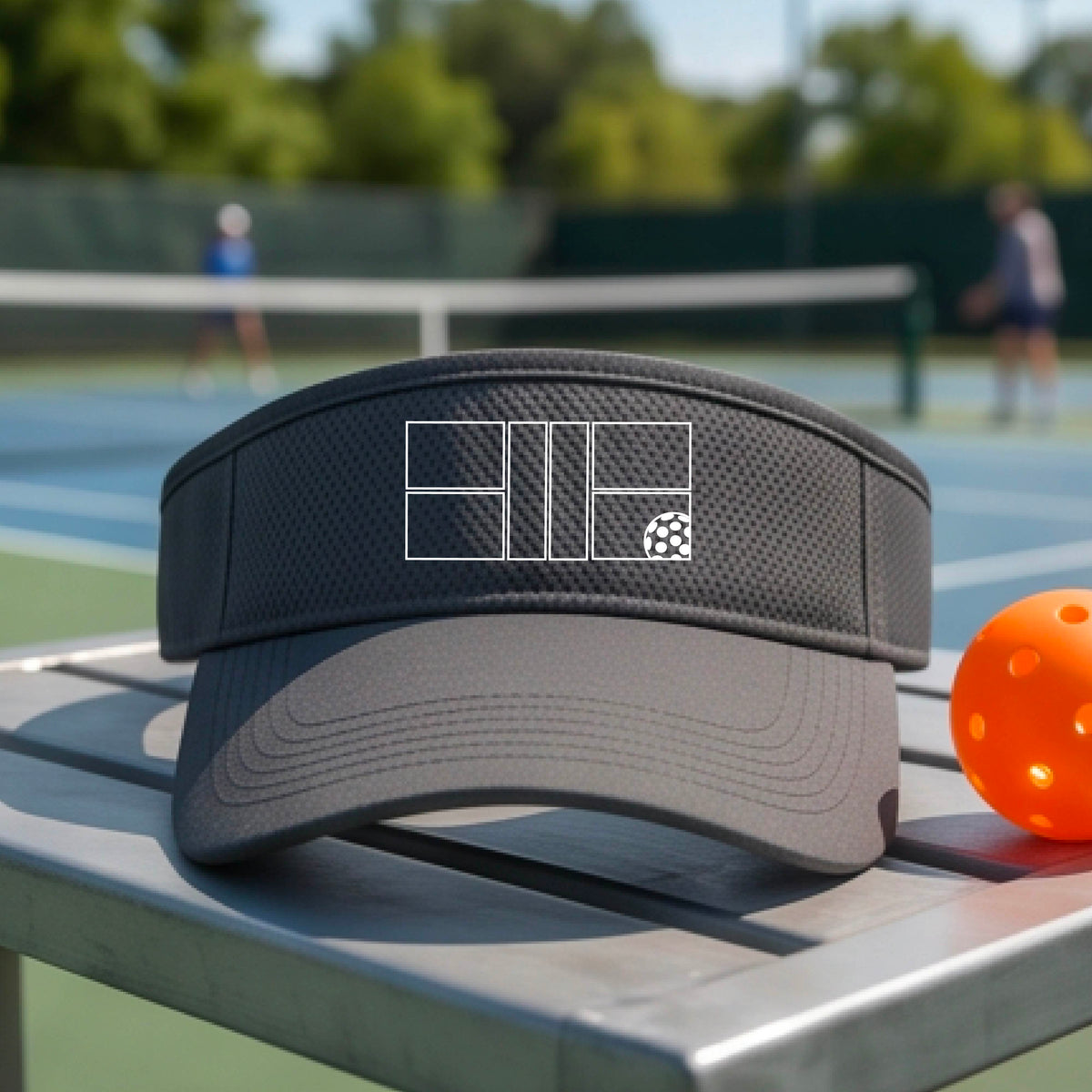 A close up of a graphite gray visor with a white pickleball court and ball graphic on the front. 