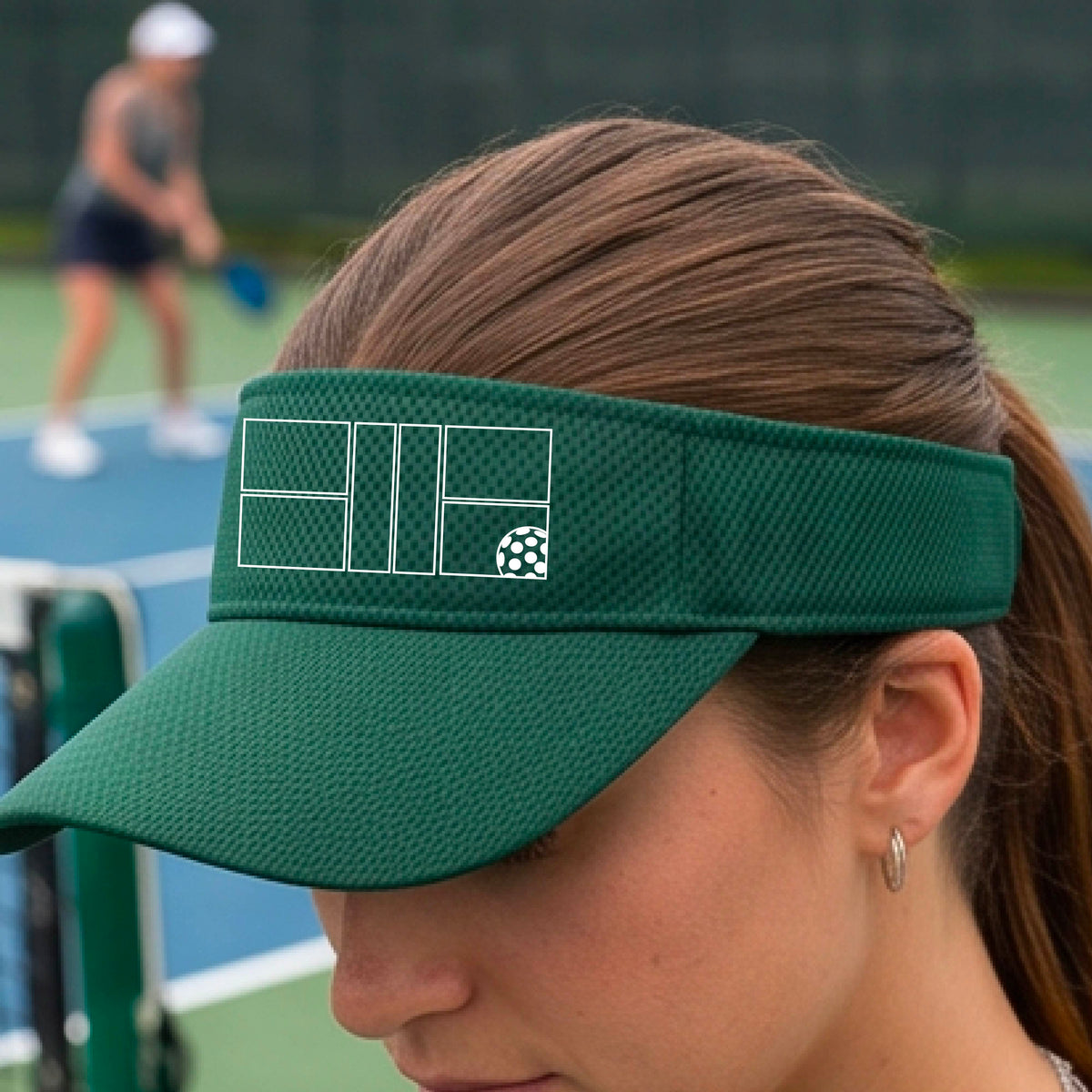 A close up of a green visor with a white pickleball court and ball graphic on the front. 