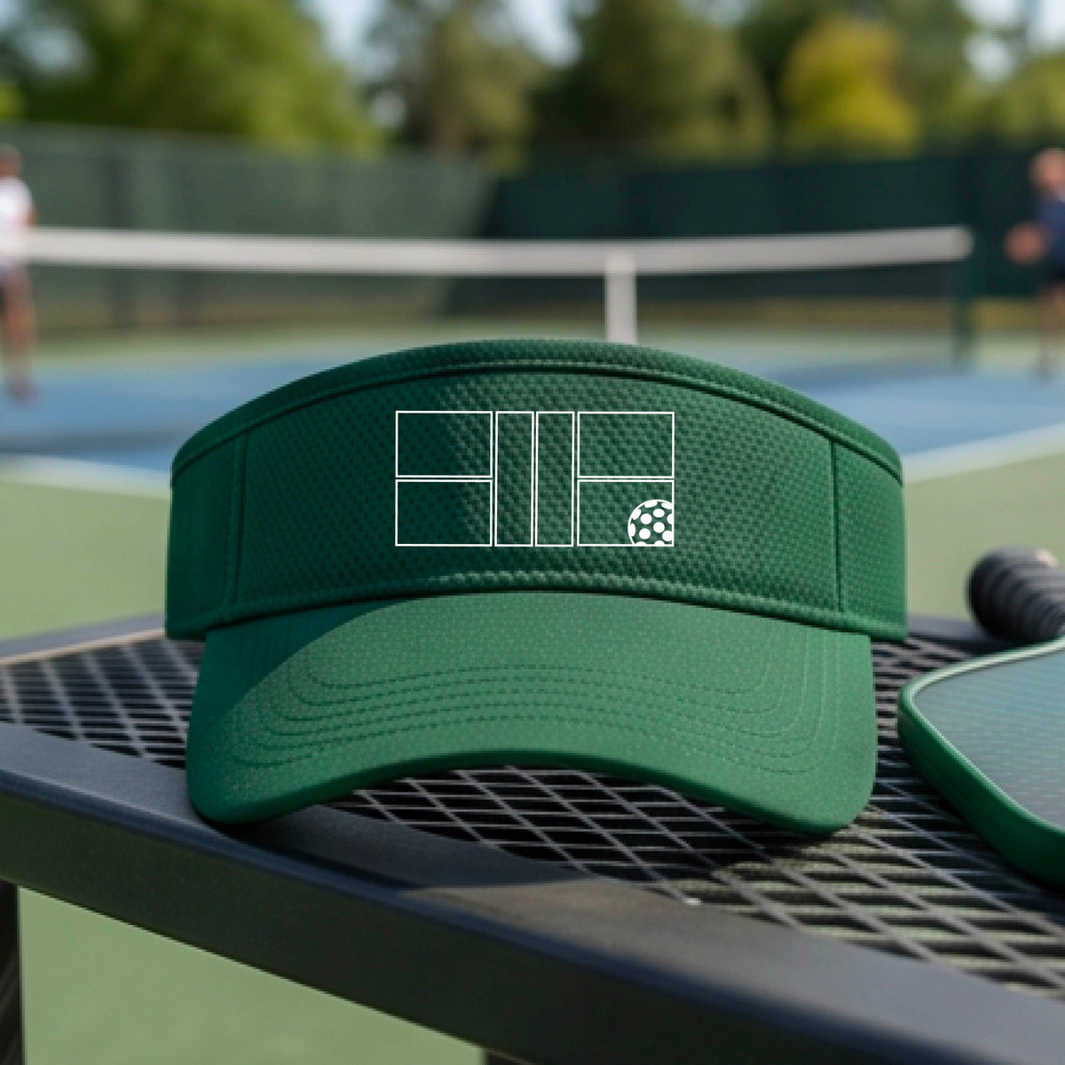 A close up of a green visor with a white pickleball court and ball graphic on the front. 